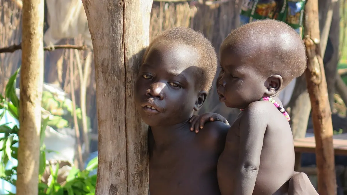 One child carrying another child on their hip standing among trees.